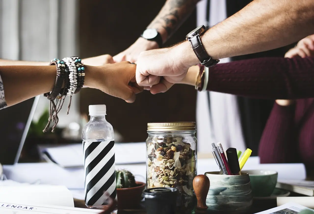 Team members joining hands in a fist bump over a desk, a symbol of collaboration