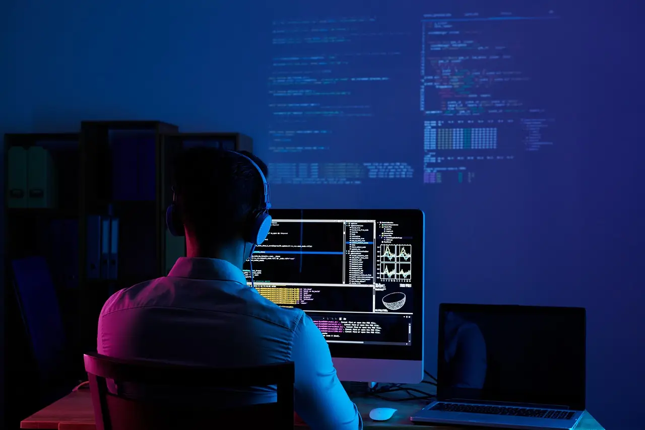 Software developer working at multiple monitors showing code