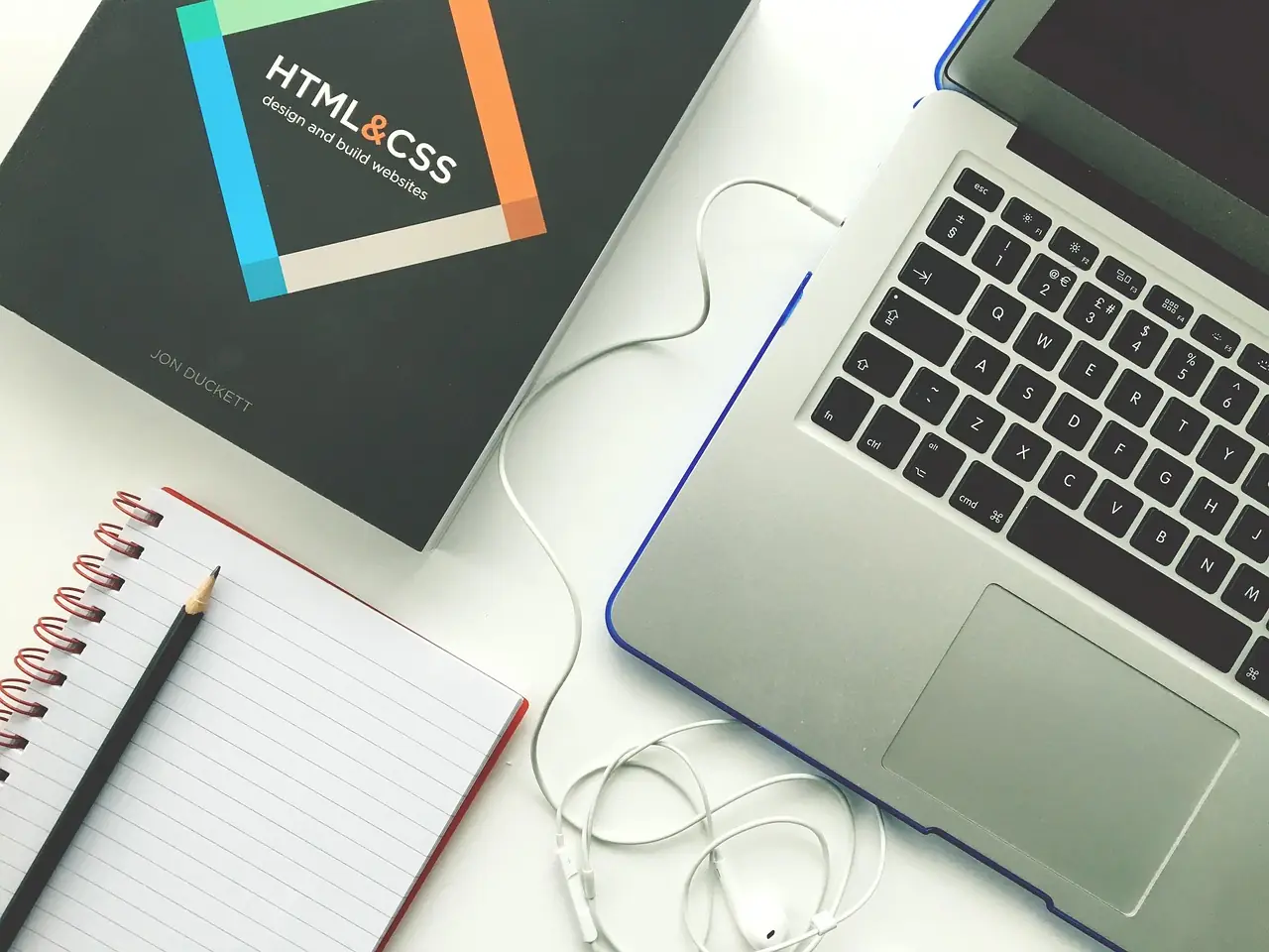 Laptop beside an HTML and CSS design book and a notebook